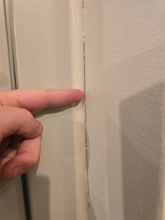 Finger pekar mot släppa fog vid balkongdörrskarm i vitmålad lägenhet.