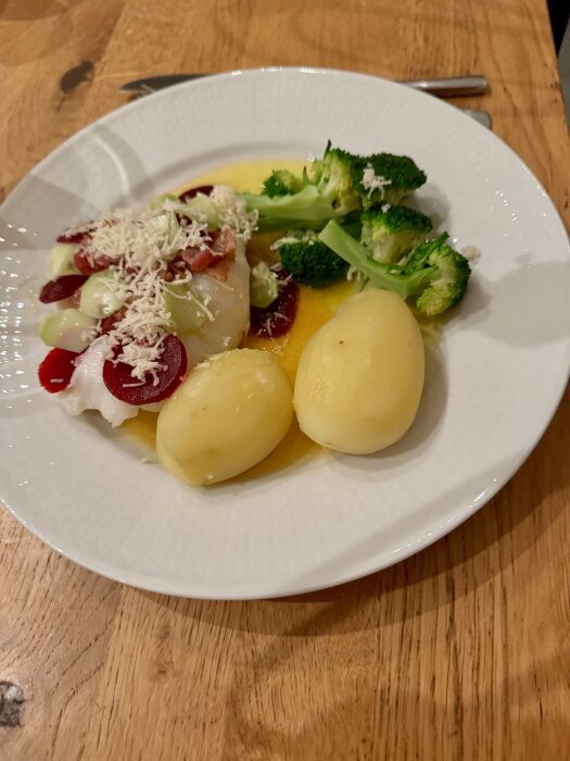 Tallrik med torsk, kokt potatis, broccoli och smält smör, garnerad med rödbetor och pepparrot.