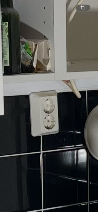 Utanpåliggande dubbeluttag monterat på svart kakel med synlig hålighet ovanför.