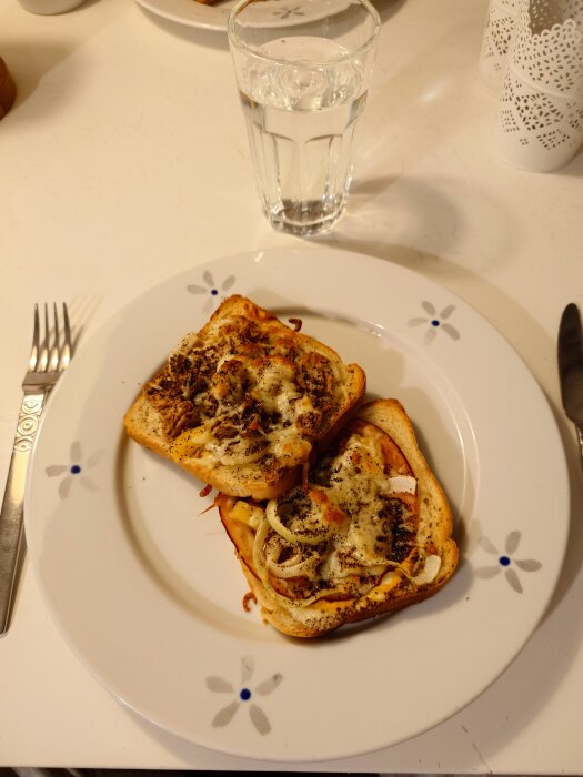 Två varma mackor på vitt porslin, en med skinka och en med tonfisk, serverade med ett glas vatten.