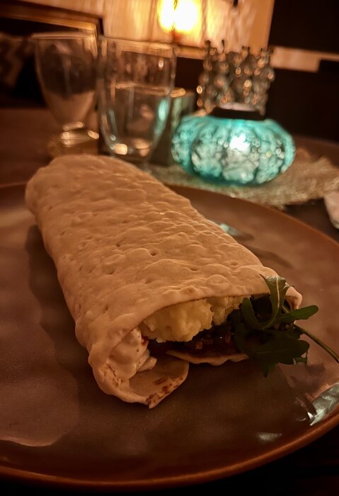 Tunnbrödsrulle med ruccola, kabanoss, räksallad, mos, rostad lök, bostongurka, ketchup och senap serverad på en tallrik i mysig belysning.