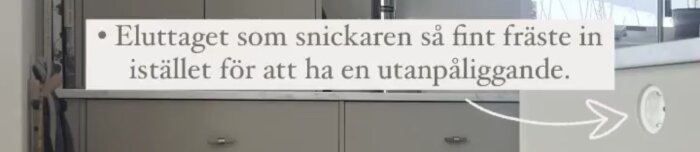 Infräst eluttag på köksö gavel, diskret integrerat i täckskiva med text om snickarens arbete och pil som pekar på uttaget.