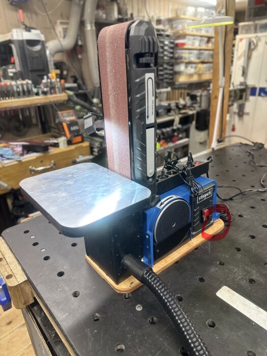 Scheppach band- och tallriksslip BTS900 på arbetsbänk, med fokus på vertikal bandslip och stort metallbord i verkstadsmiljö.
