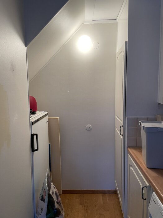 Vägg mellan kök och vardagsrum med lampa och lampknapp i ett trångt utrymme, före planerad rivning för att öppna upp rummet.
