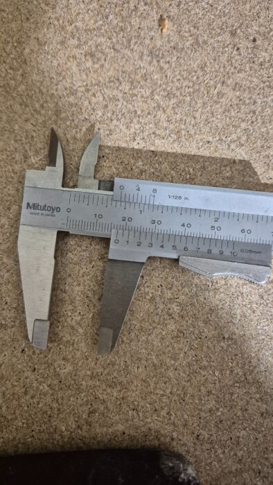 Skjutmått på en spånskiva, visar millimeter och tum-skala. Används för att mäta avstånd på rör i projektet med gamla radiatorer.