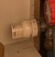 Begränsningstermostat installerad på ett rör i ett skåp, potentiellt för att reglera temperaturen och skydda mot överhettning av trägolv.
