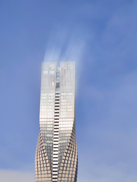 Skyskrapa med modern design mot en klarblå himmel, med reflekterande glasfasad och en unik böjd form.