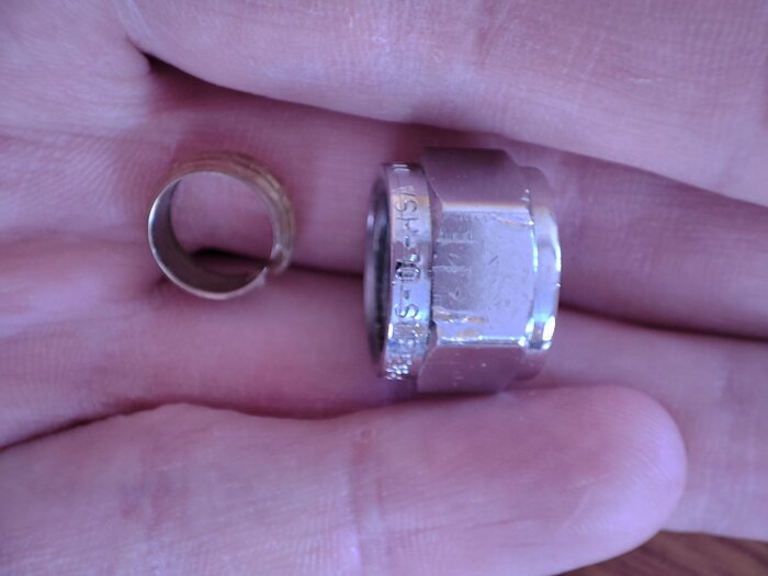 Koppar klämring och metallmutter ligger i en persons hand, relaterade till VVS-problem vid byte av blandare.