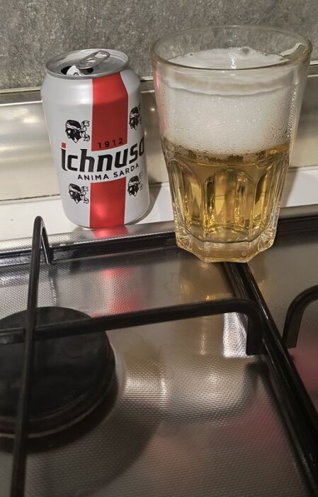 Burk med "Ichnusa" öl och ett glas lager på en spishäll.
