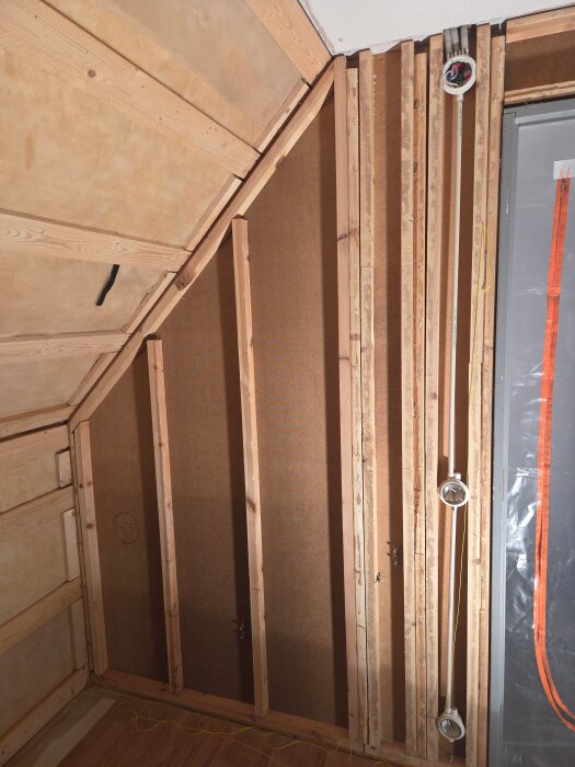 Ojämna träreglar på en innervägg, del av pågående renovering där masonitskivor ska bytas mot gips. Synliga elkablar längs väggen.
