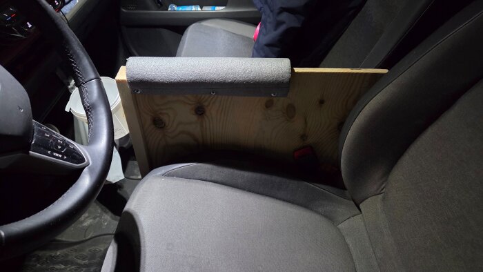 Självtillverkat armstöd i trä och skumgummi installerat mellan sätena i en bil, prototyp på hemmabyggd lösning.