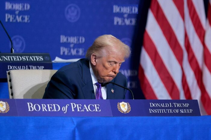 Man i kostym sitter vid bord med text där det står 'Bored of Peace' och 'Donald J. Trump Institute of Sleep' framför en amerikansk flagga.