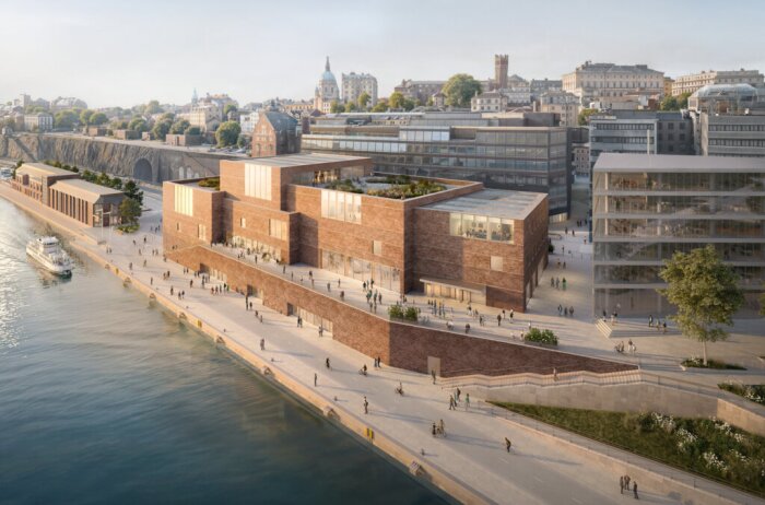 Nobelcenter vid strandpromenad i Stockholm, tegelbyggnad med glasdetaljer, människor på gångväg och cykelbana, solbelyst miljö med vatten i förgrunden.