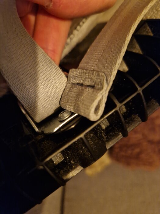 Bilden visar en rem i ett snabblås på en bilbarnstol, med remmen löst hängande och inte öglad.