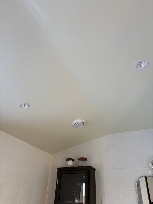 Nymålat badrumstak med gulnad färg, vita kakelväggar och infällda spotlights.