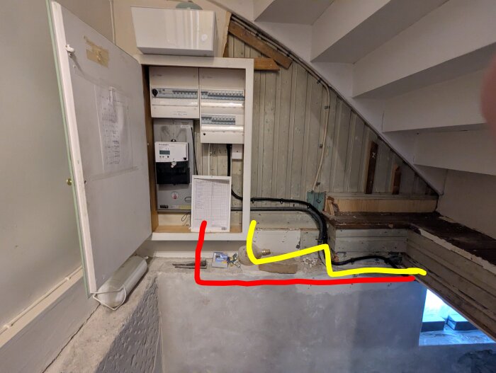 Elskåp under trappa med röd och gul linje markerade på väggen bredvid.