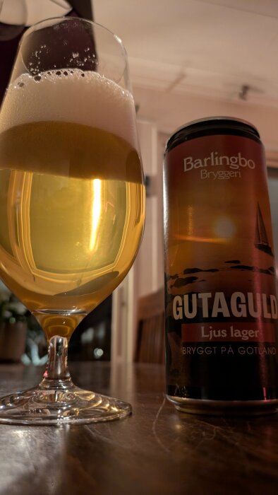 Ett glas ljus lager från Barlingbo Bryggeri och en burk Gutaguld på ett träbord inomhus.