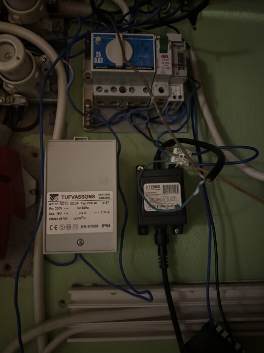 En elektrisk installation med säkringar, kablar och utrustning från Tufvassons och S:t Eriks, placerad mot en grön vägg.