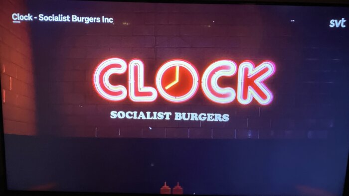 Neonskylt med texten "CLOCK SOCIALIST BURGERS" på en tegelvägg under ett TV-program på SVT.