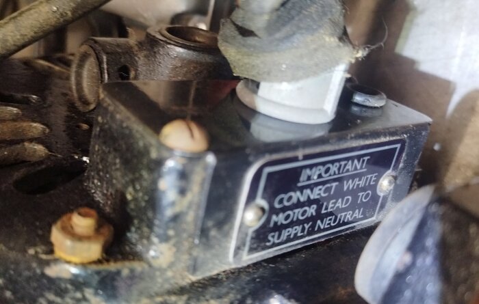 Närbild på gammal elektrisk komponent med instruktion om att koppla vit motorledning till jordad anslutning.