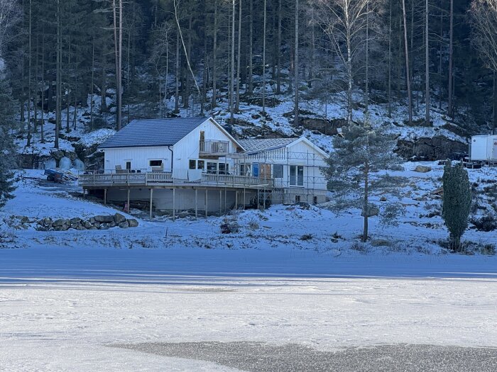 Hus med ny fasad under vintertid, omgiven av snö och skog.