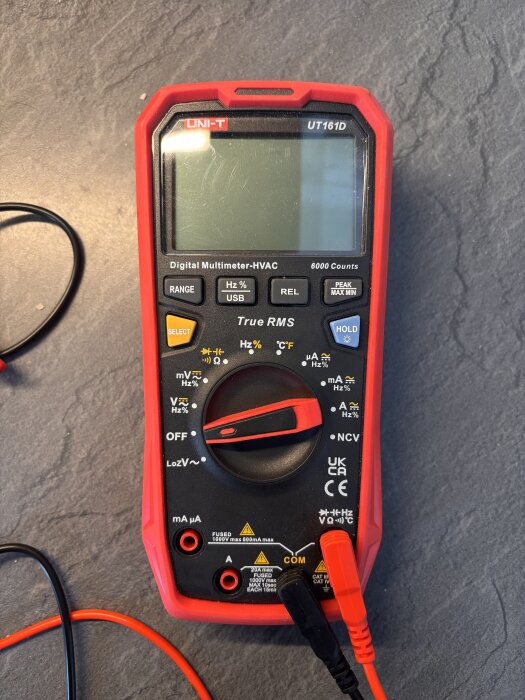Multimeter UNI-T UT161D med röda och svarta kablar på ett grått underlag, använd för att felsöka elektriska problem.