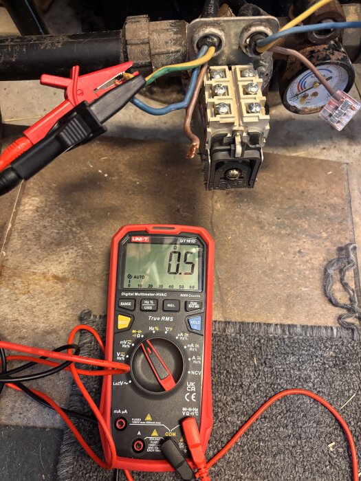 Multimeter visar 0,5 volt med kopplingar mellan elledningar vid ett kopplingsblock, misstänkt mörk anslutning.