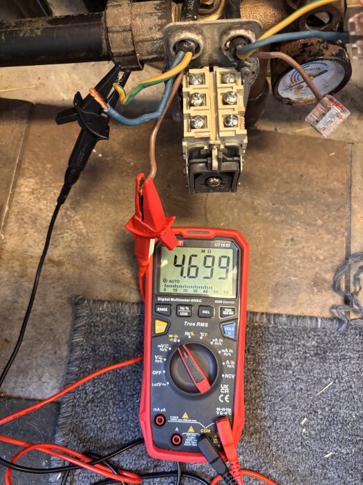 Multimeter visar 4699 MΩ mellan fas- och jordledningarna, med kablar anslutna till ett eluttag.