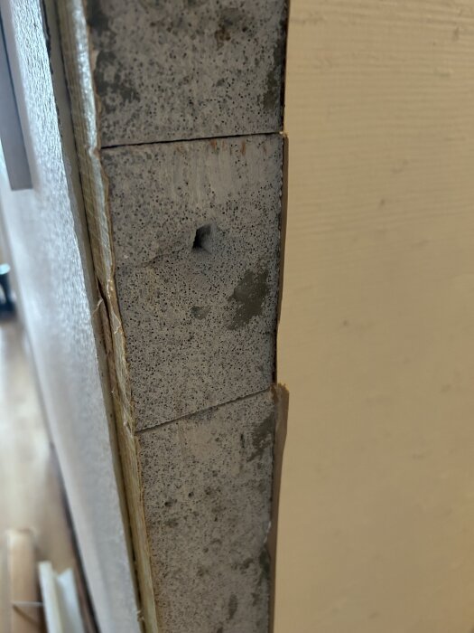 Närbild av oanstruken lättbetongvägg med en borrad hålighet, del av ett 60-talshus, möjligtvis blåbetong enligt text.