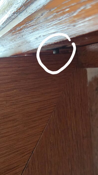 Gångjärn med liten stav som inte fäster i hålet på toppskivan i ett gammalt skåp, markerad med en vit cirkel.