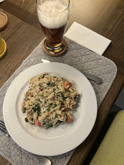 Risotto med svamp, lök, spenat, körsbärstomater, parmesan, strimlad salami och chilipeppar på en tallrik, med ett glas öl bredvid.