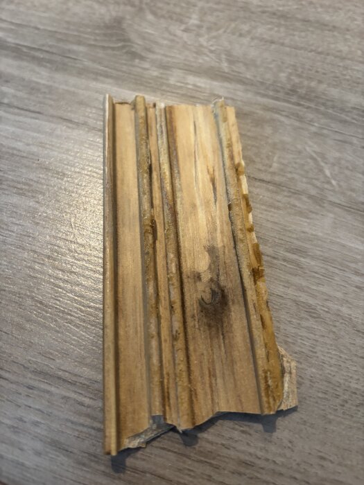 Bruten tröskelbit av trä på ett golv, borttagen som en del av renovering; behöver lösning för att återställa den med dörrkarmen.