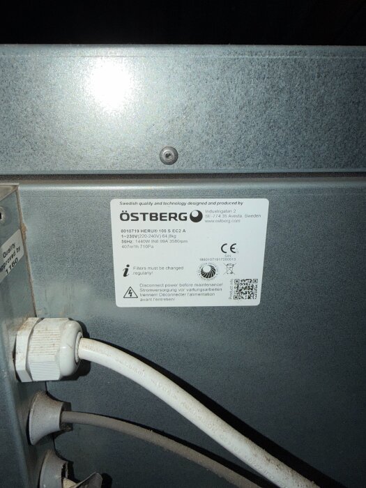 Etikett på en fläkt från Östberg med tekniska specifikationer och säkerhetsinformation. Kabel synlig under etiketten.