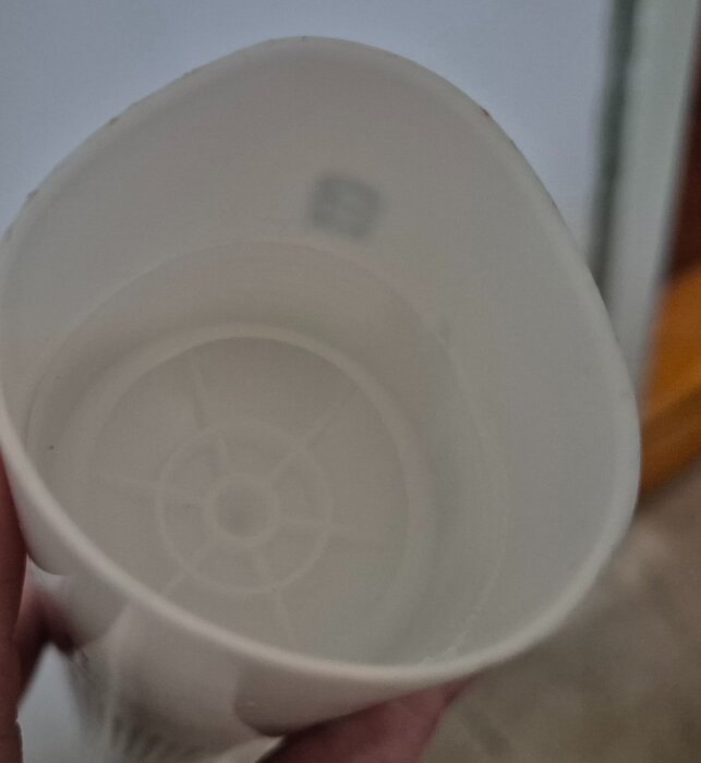 Plastbehållare uppifrån med runda strukturer i botten och delvis synlig inre design, hålls i en hand.