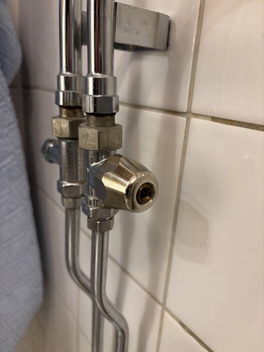 Handdukstorkventil med två rör och en sexkantig vred på kaklad vägg.