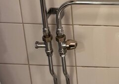 Kromade rör och ventiler i badrum med handdukstorkanslutning och vred på en vit kakelvägg.