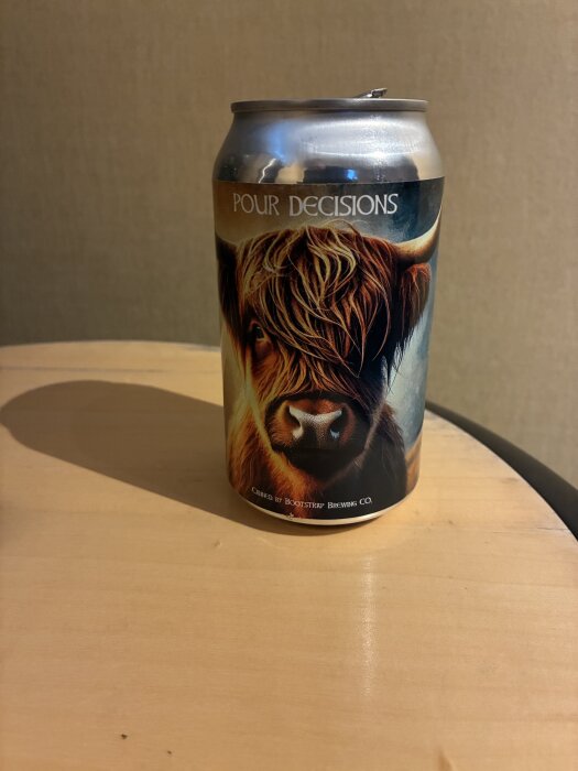 En ölburk från Bootstrap Brewing med en bild på en ko på etiketten, märkt "Pour Decisions", står på ett bord.