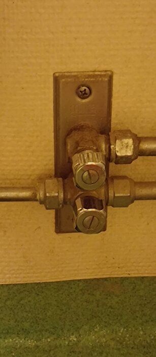 Gammalt väggmonterat vattenrör med två avstängningsventiler i metall med spår för skruvmejsel.