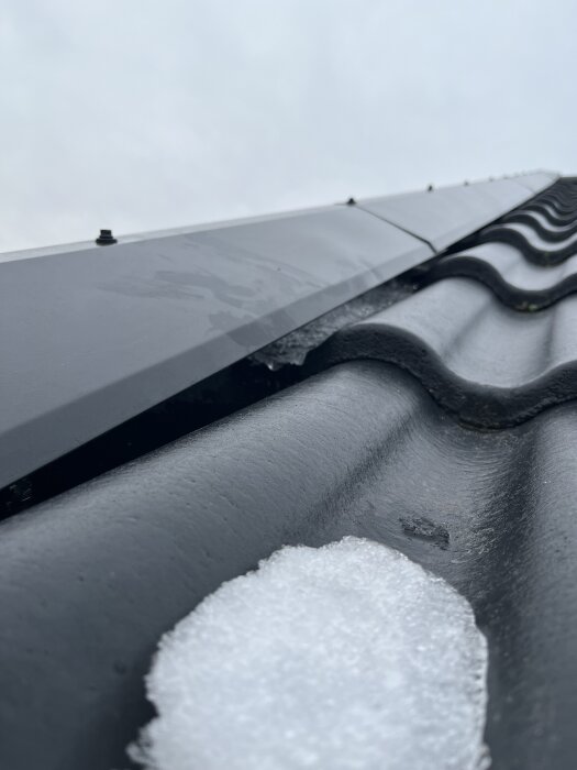 Snö på takpanna nära vindplåt, potentiellt läckage synligt. Fråga om snöns påverkan och möjliga åtgärder för att förhindra att vatten når läkten.