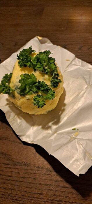 Smörkula dekorerad med färsk persilja på ett papper mot en träyta.