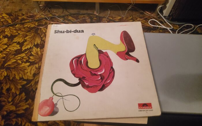Vinylomslag med surrealistisk illustration av ett ben i gul strumpa och röd sko som sticker ut ur en rosa ros, skivmärke Polydor i hörnet.