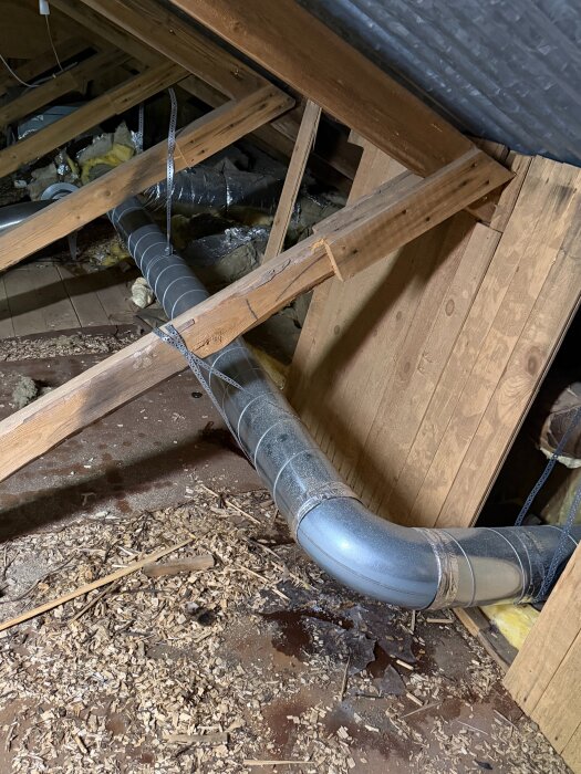 Oisolerade ventilationsrör i en vind med träbjälkar och spånskivor, rör sammanfogat med annan isolerad sektion.