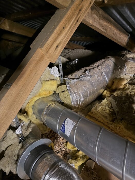 Oisolerade ventilationsrör i en vind med träkonstruktion och isolering. Ett av rören är hopkopplat med en isolerad del.