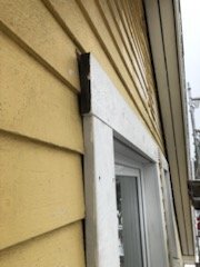 Gult trähus med fönster utan överbleck, fånget från sidan på norrsidan, synlig väderpåverkan, snickarens foto med suddig kvalitet.