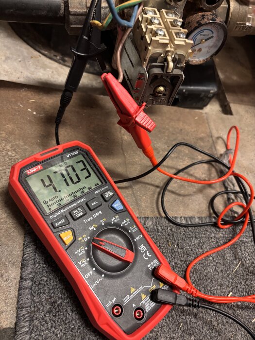 Multimeter med röda och svarta kablar mäter resistans mellan fas och jord (~4,7 MOhm) på en ansluten kabel i en mekanisk installation.