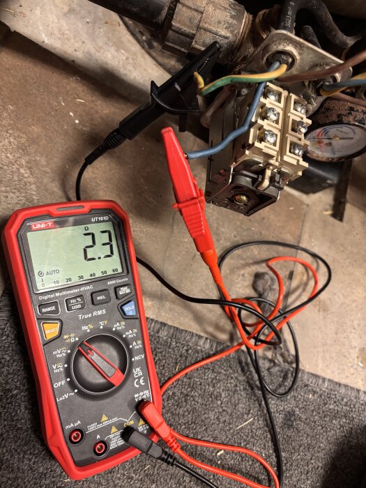 Digital multimeter visar 2,3 Ohm vid mätning av kablage nära pumpinstallation, med röd och svart mätspets anslutna till terminalblock.