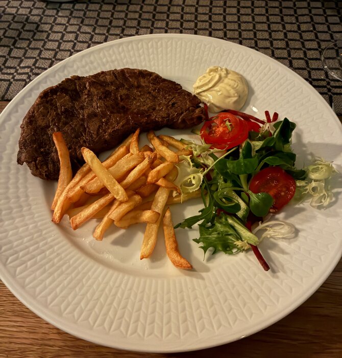 Grillad ryggbiff med pommes frites, sallad med tomater och en klick bearnaisesås på en tallrik.