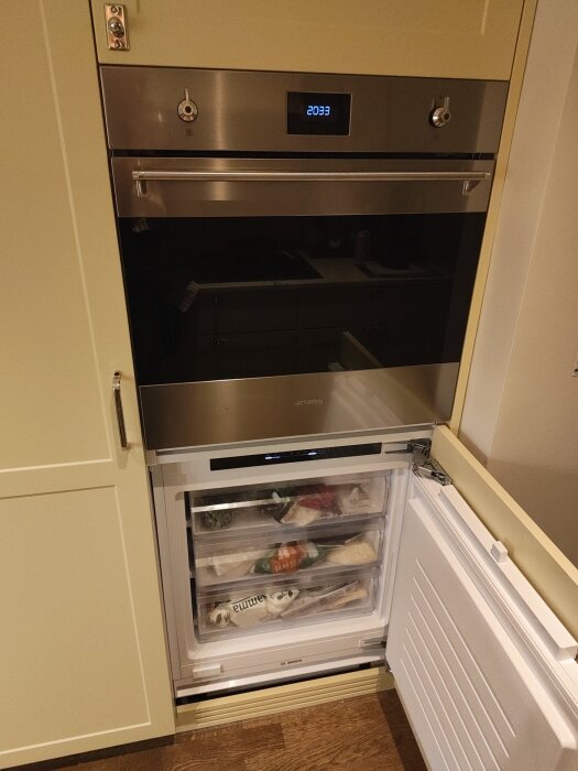 Inbyggd frys och ugn i modifierad IKEA-stomme, med öppen frysdörr som visar lådor fyllda med matvaror.