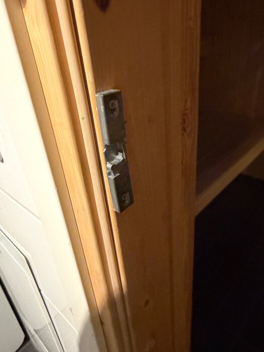 Närbild av en trädörr med en synlig metallåsplatta fäst vid kanten, bredvid ett kaklat väggparti.