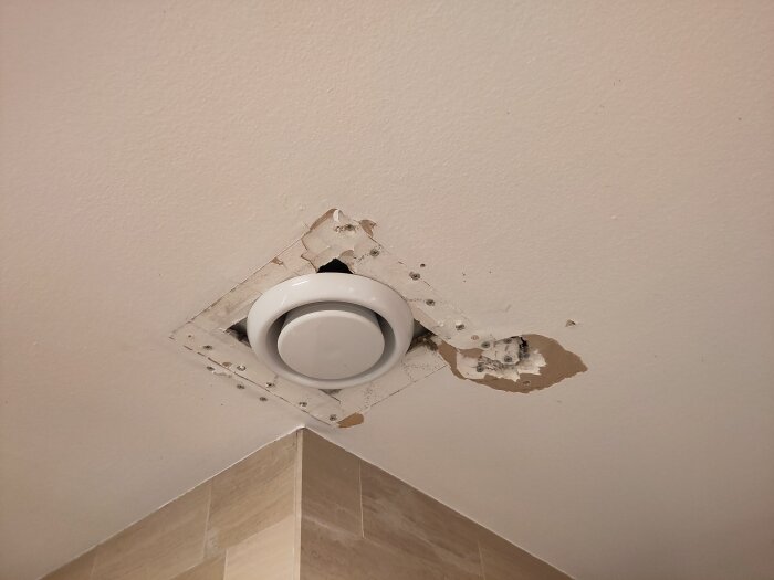 Ventilationsventil installerad i ett tak med märken från tidigare montering runt hålet.